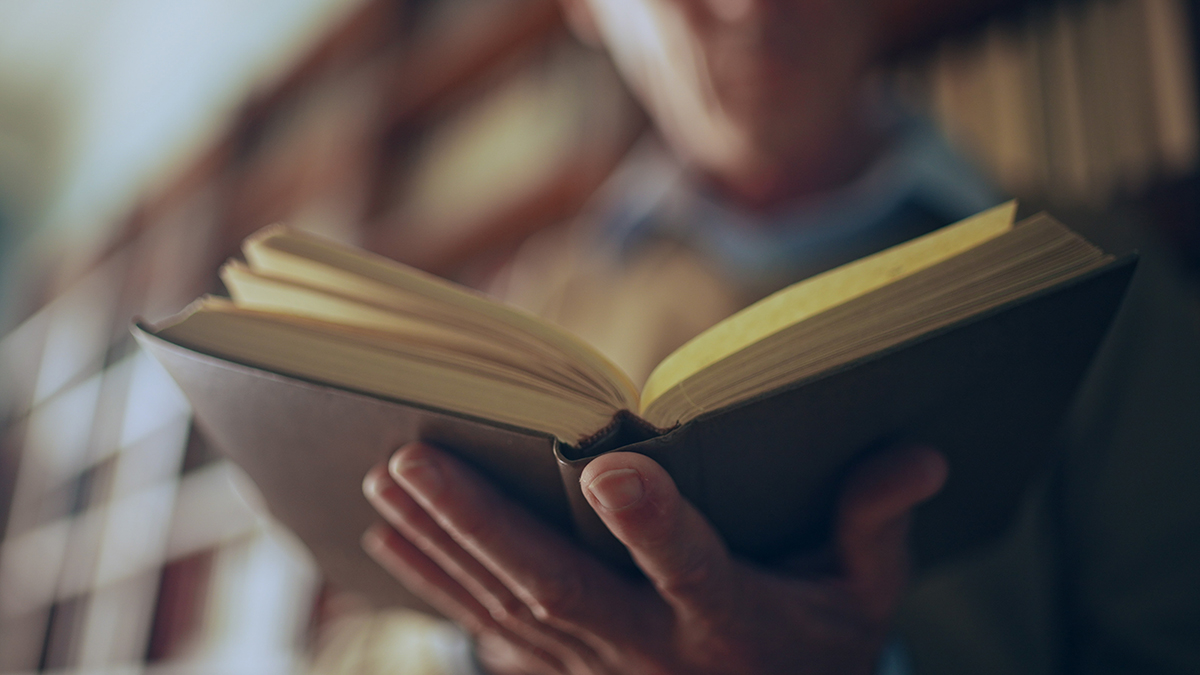 A blurred person is reading from an open book.