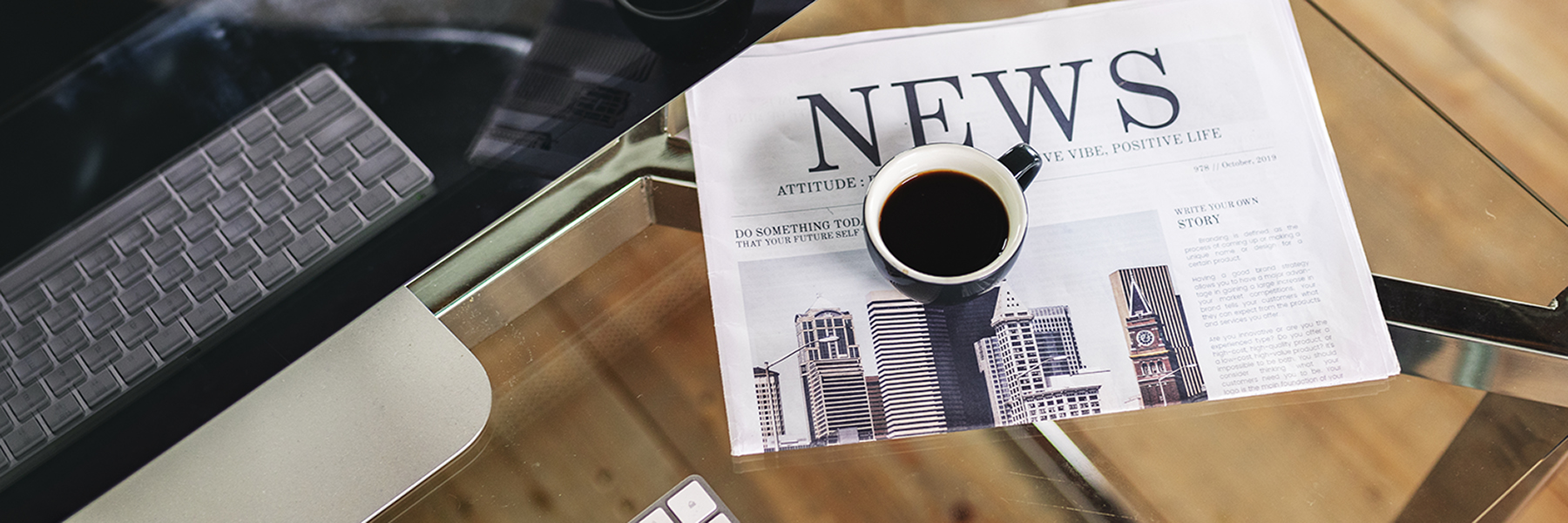 A coffee cup sits on top of a newsletter on a desk, beside a computer.