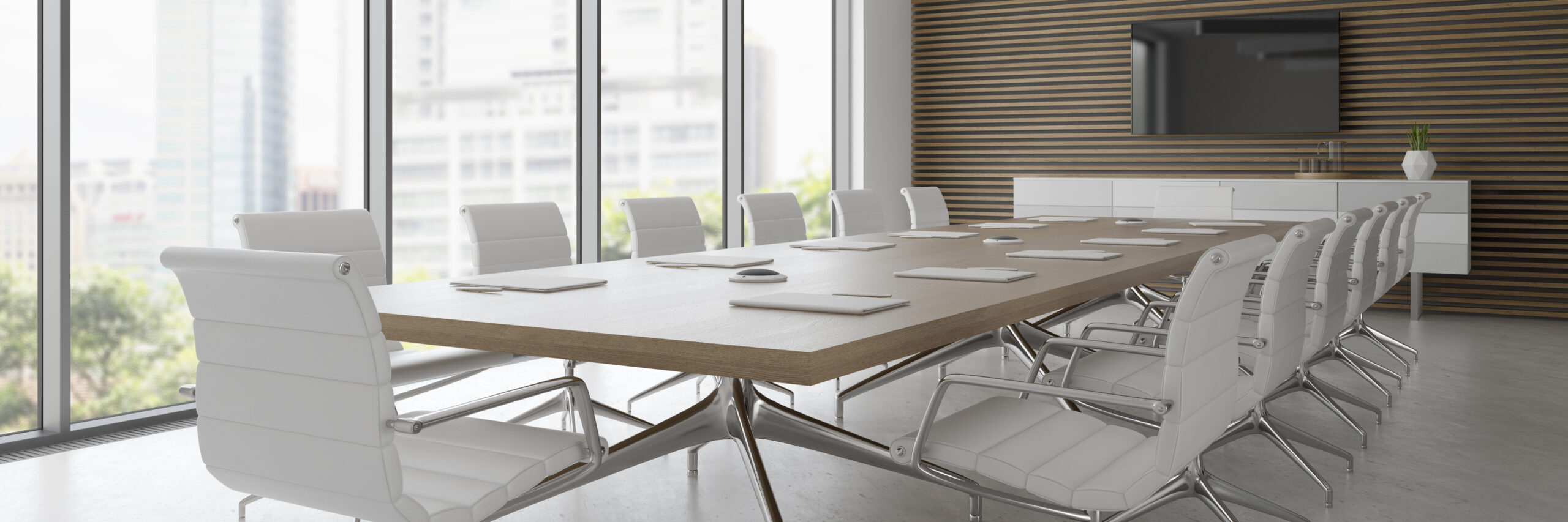 A boardroom table with white chairs in front of a window.