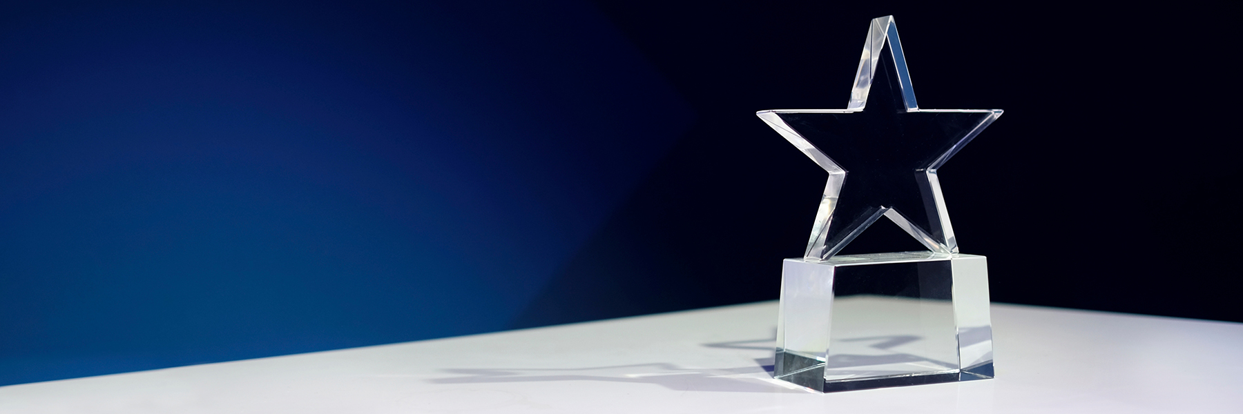 A transparent star-shaped trophy sits on a table, against a blue background.